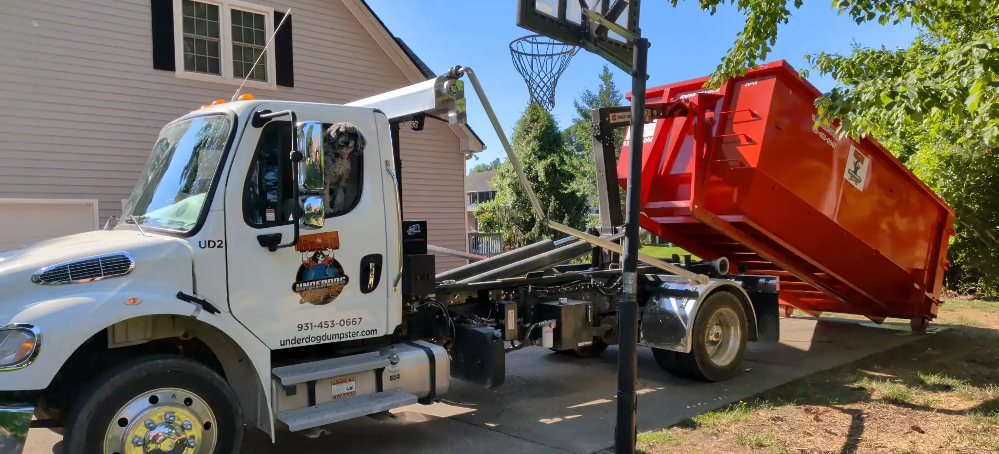 Underdog Dumpster truck rolling a red dumpster off onto the driveway of a Clarksville home