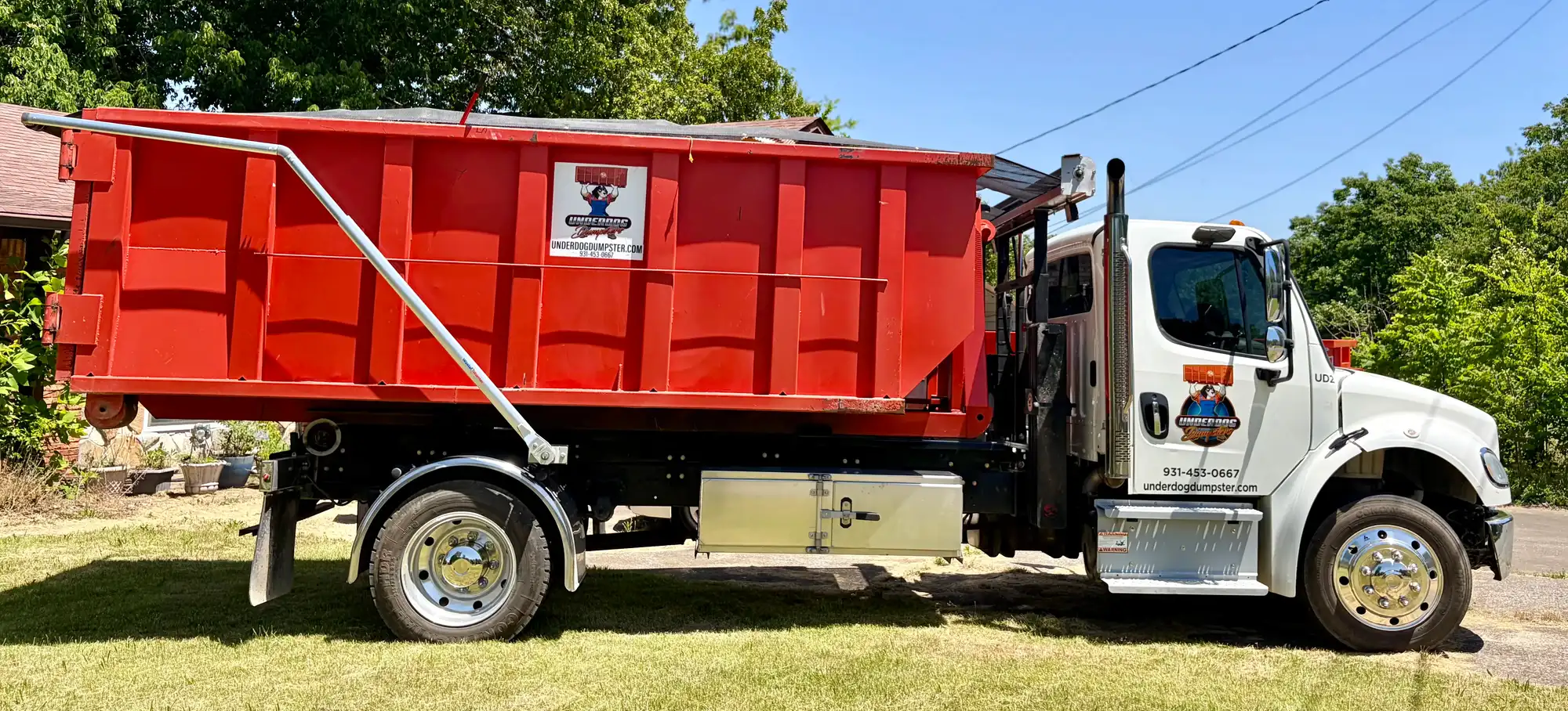 Underdog Dumpster roll-off truck setting a red dumpster down on the lawn at a Clarksville home