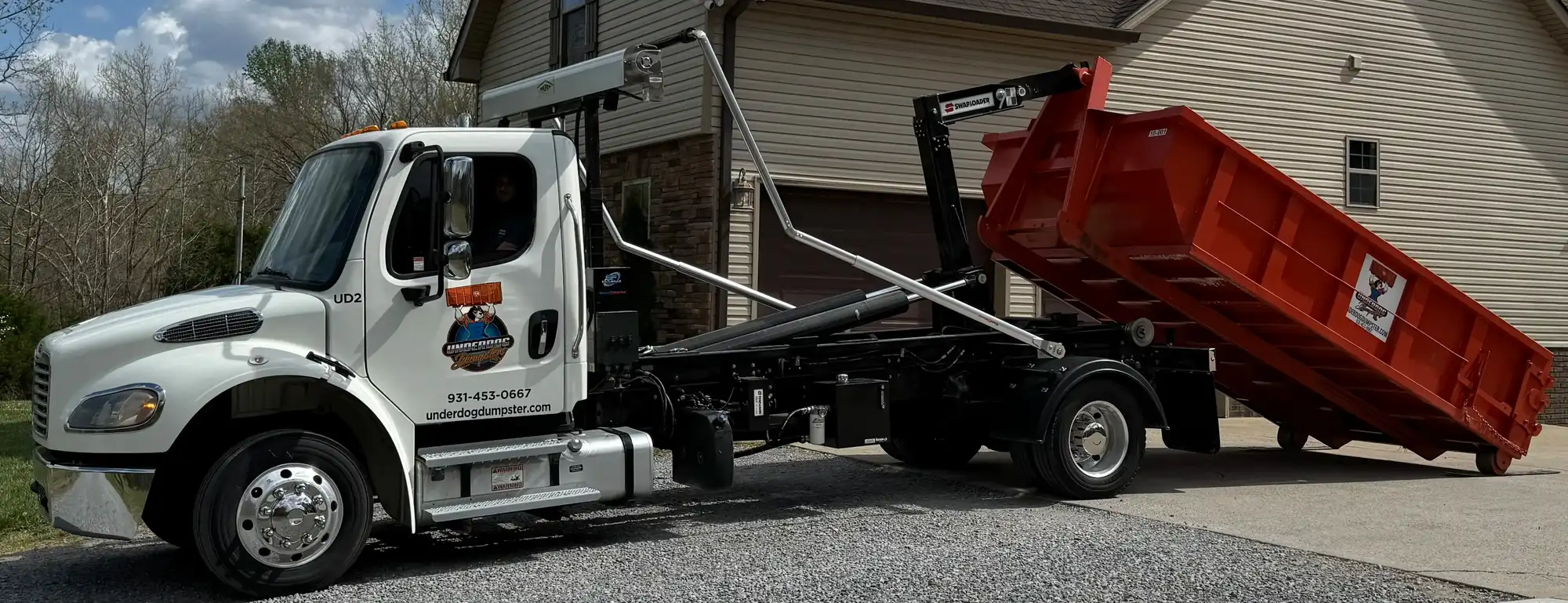Underdog Dumpster truck placing a red roll-off dumpster in the driveway of a home near Clarksville, TN