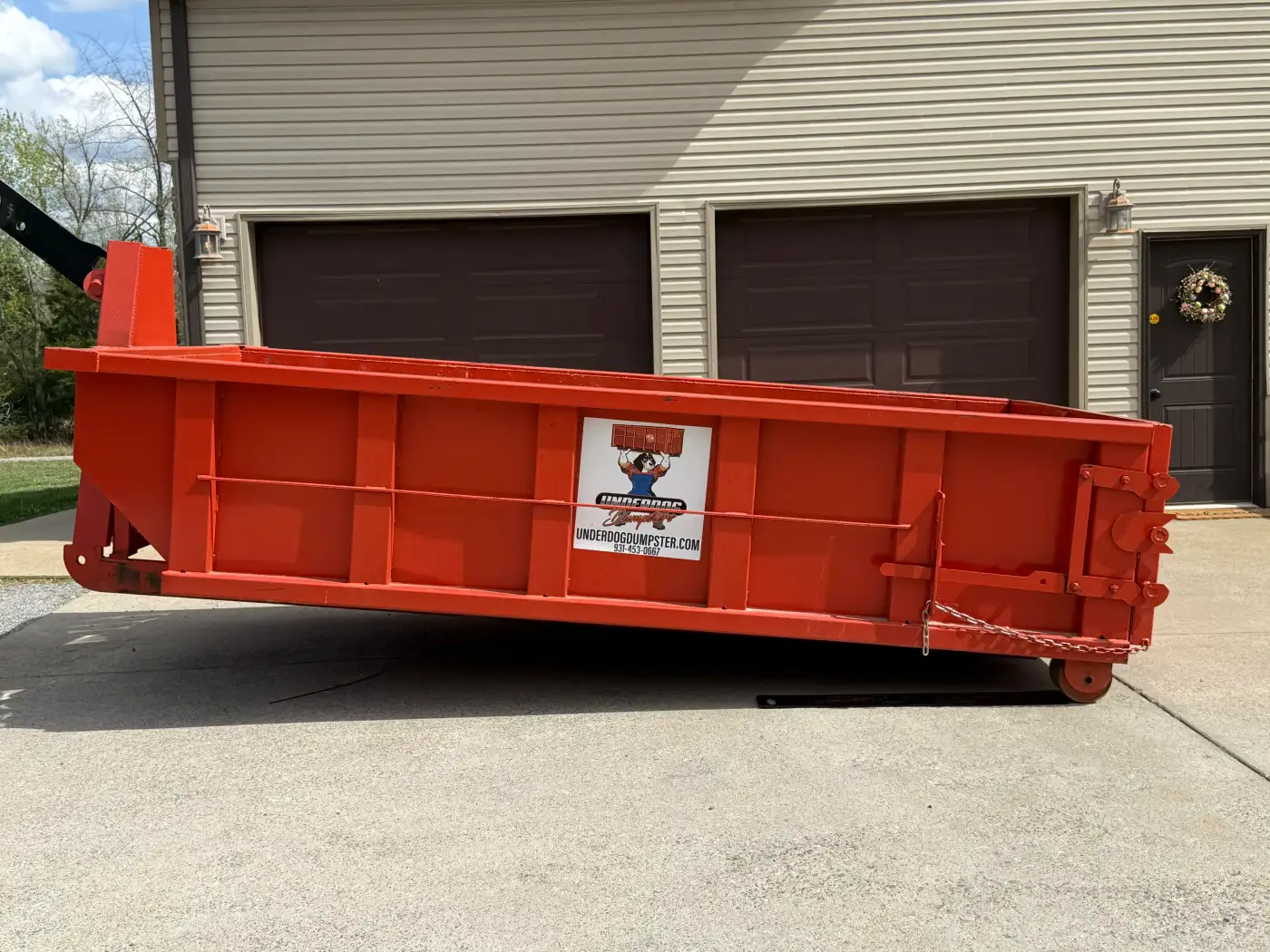 Red Underdog Dumpster 10 yard roll-off container set on a concrete driveway in front of a two-door garage at a Woodlawn, TN home