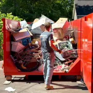 Two workers providing dumpster loading help labor, lifting junk and debris into a roll off dumpster for a residential cleanout